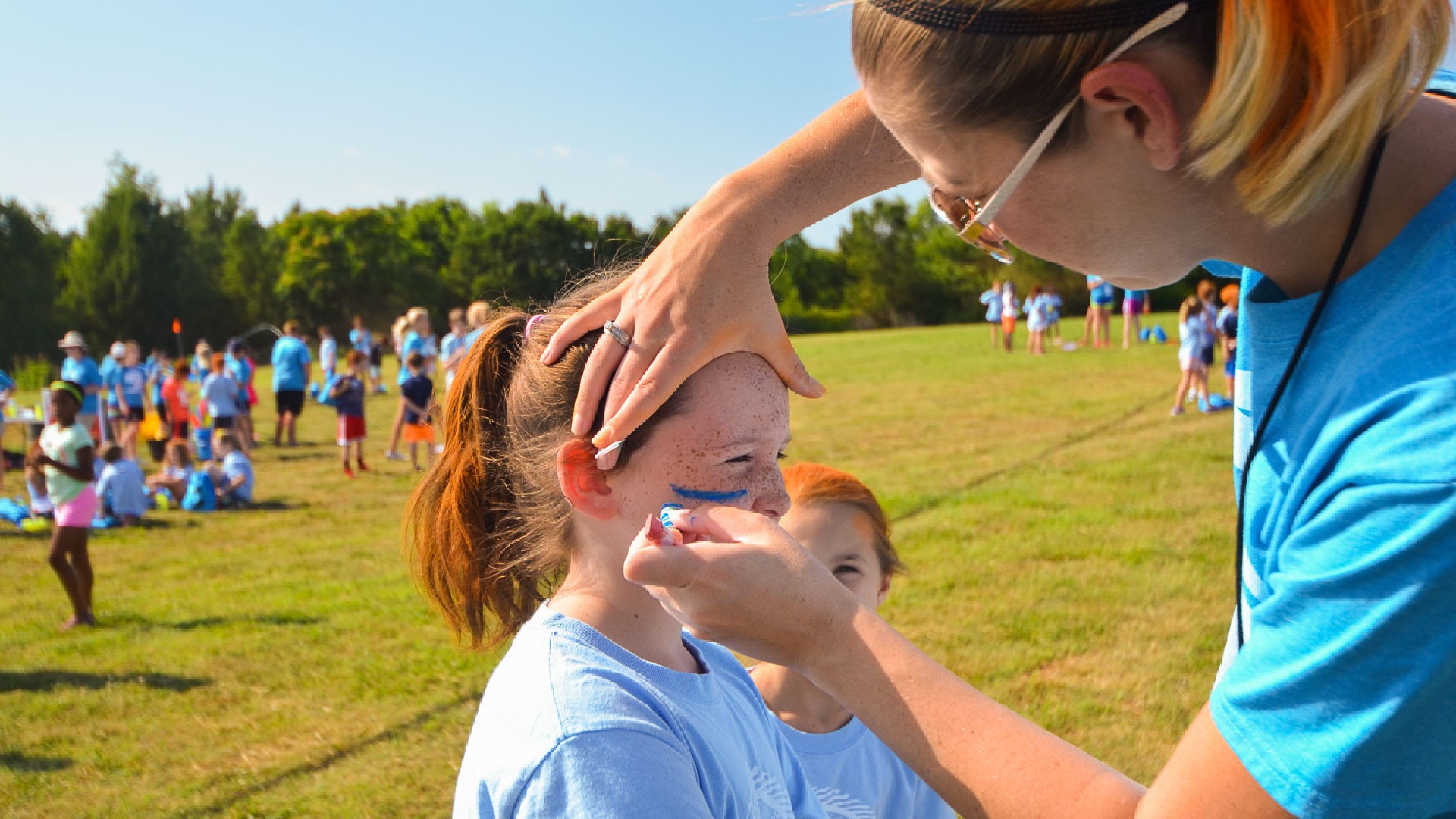 A recreation volunteer paints team colors on the faces of children at Brookwood Church